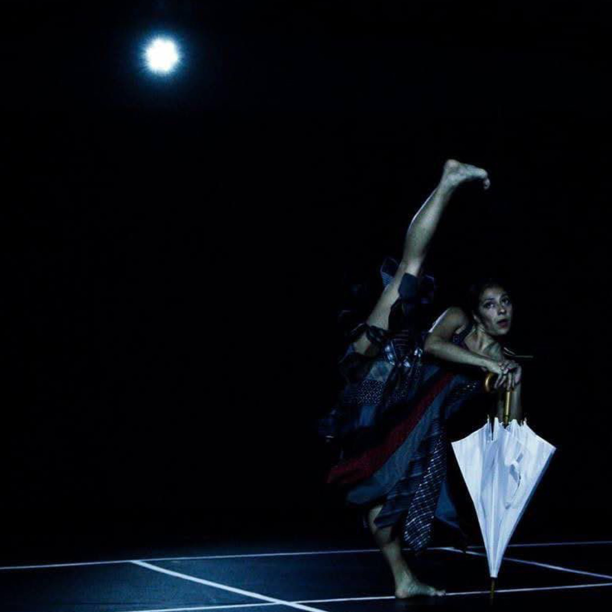 Stephanie Garcia dances on a dark stage with an umbrella 